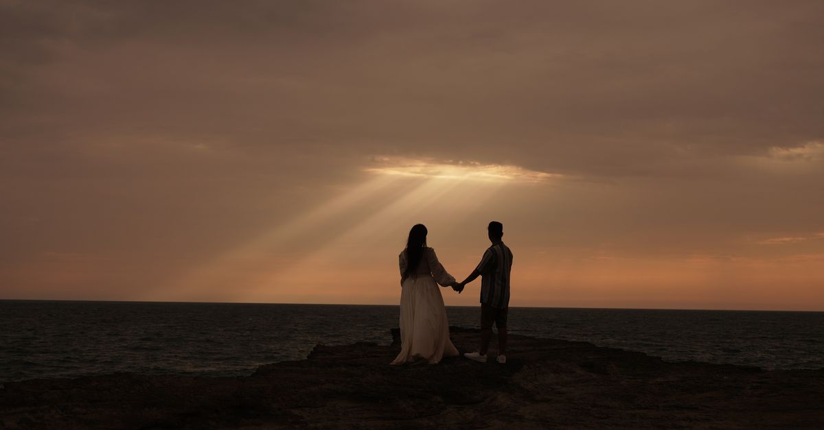 A couple holding hands at the beach during a serene sunset, creating a romantic silhouette.